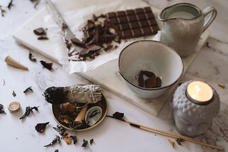 A Burnt Incense On A Round Container Beside A Chopping Board With Chocolates