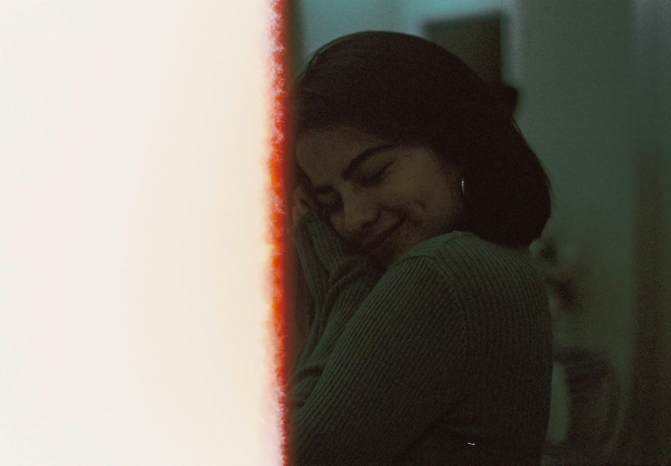 An intimate portrait of a woman with eyes closed, smiling in a warm, dimly lit indoor space.
