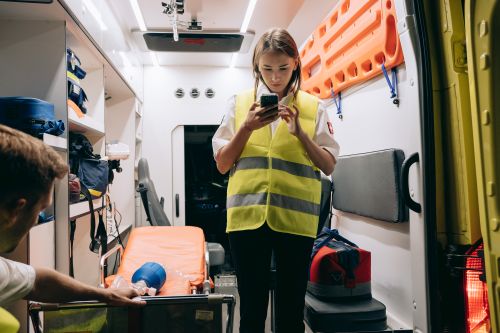 Free Female paramedic using smartphone inside an ambulance preparing for emergency response. Stock Photo