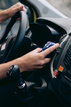 A detailed view of a person using electronics inside a car, highlighting steering and control elements.