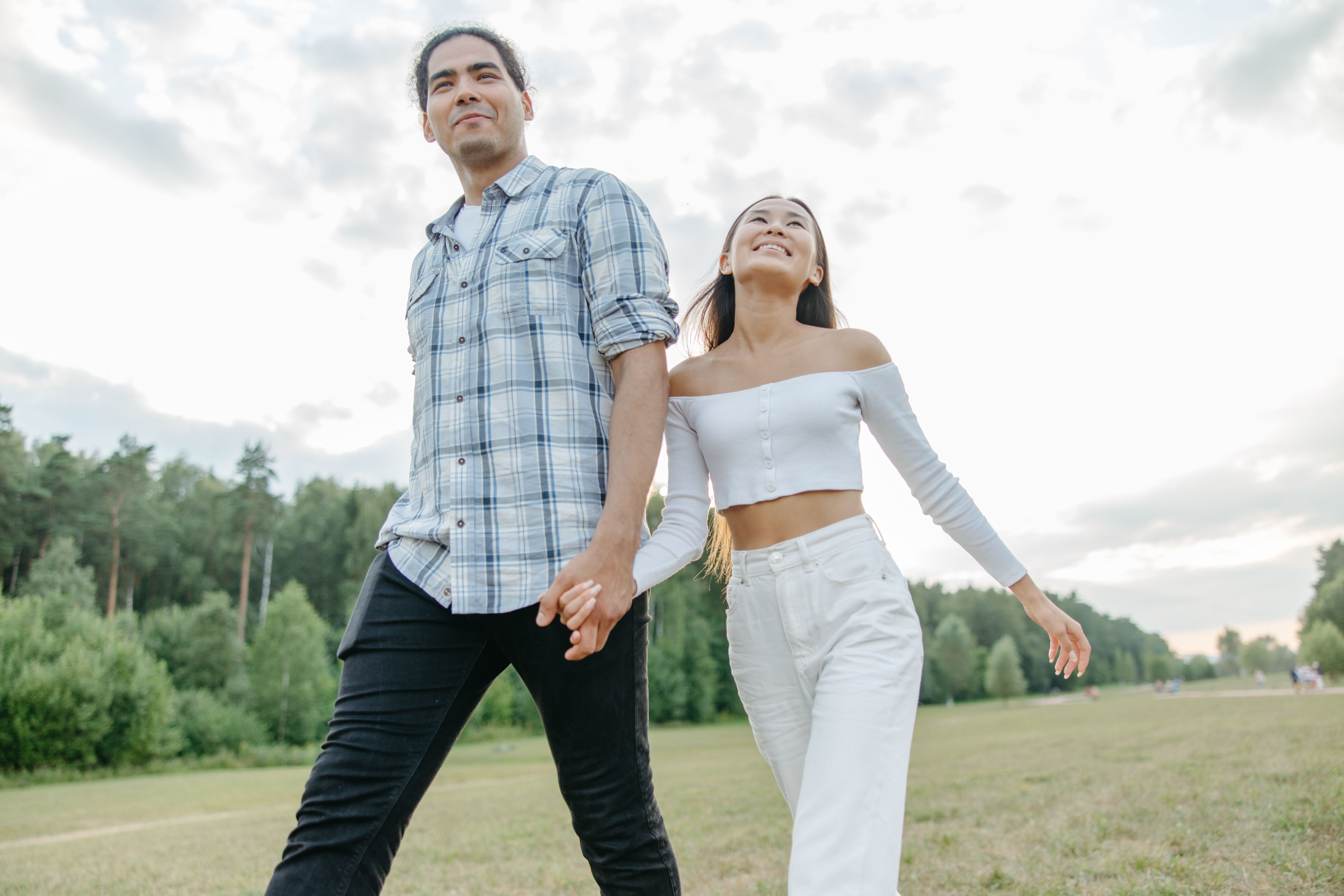 Smiling couple enjoying a walk in a sunlit park, holding hands on a summer day.
