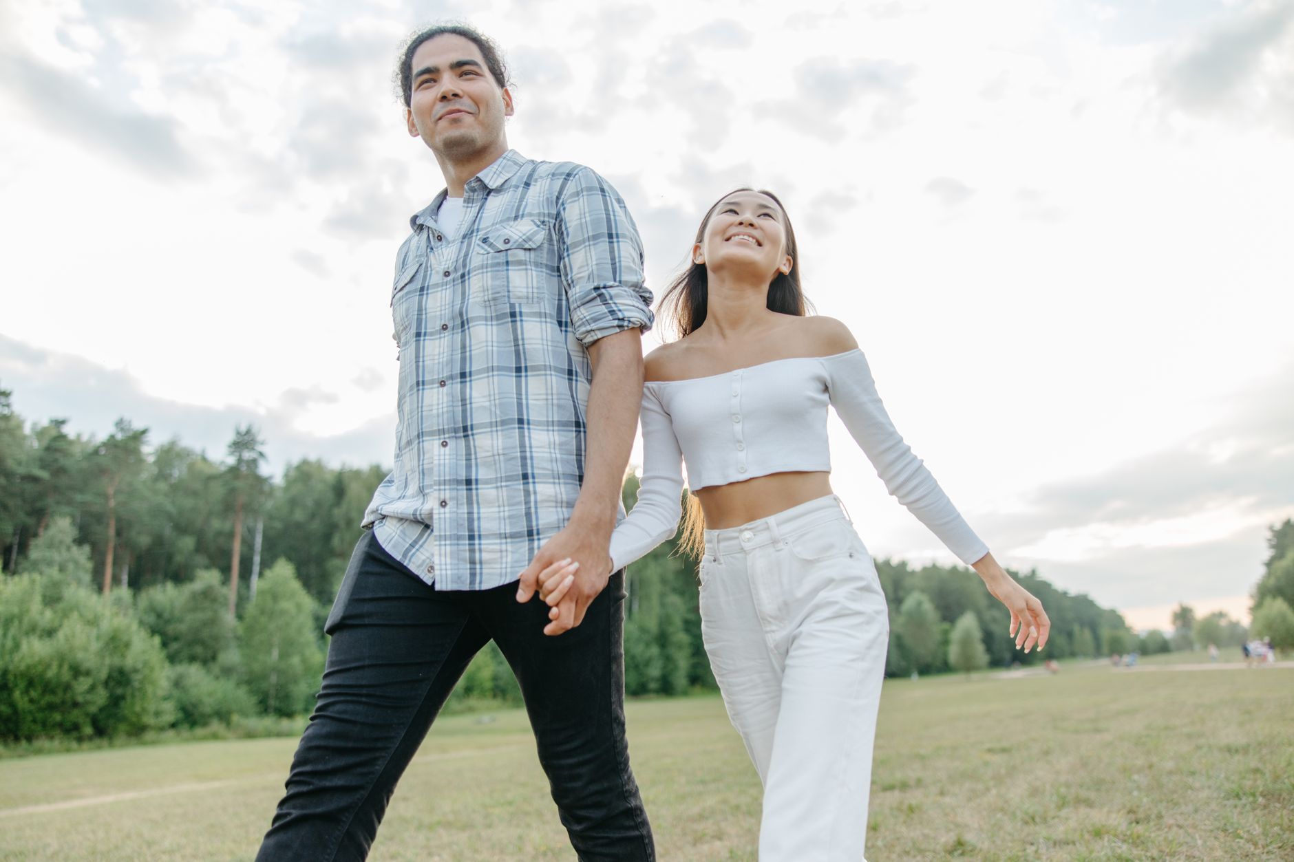 Smiling couple enjoying a walk in a sunlit park, holding hands on a summer day.