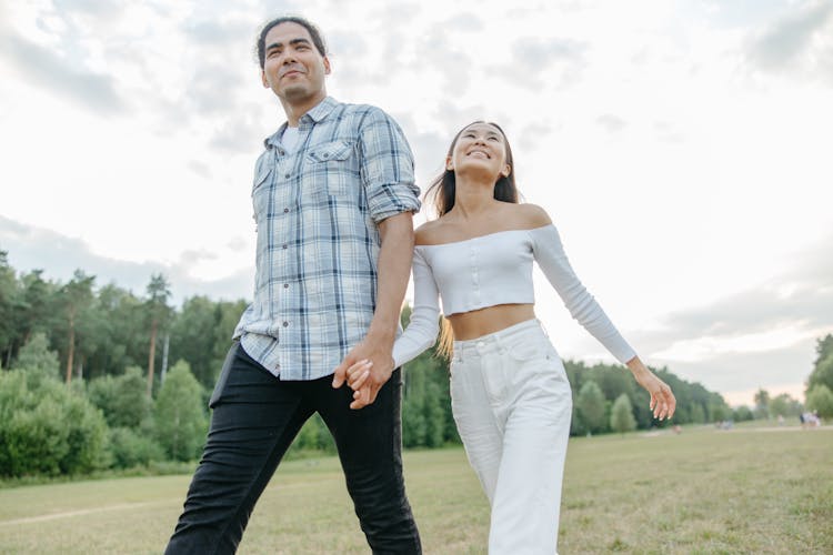 A Couple Walking On Green Grass Holding Hands