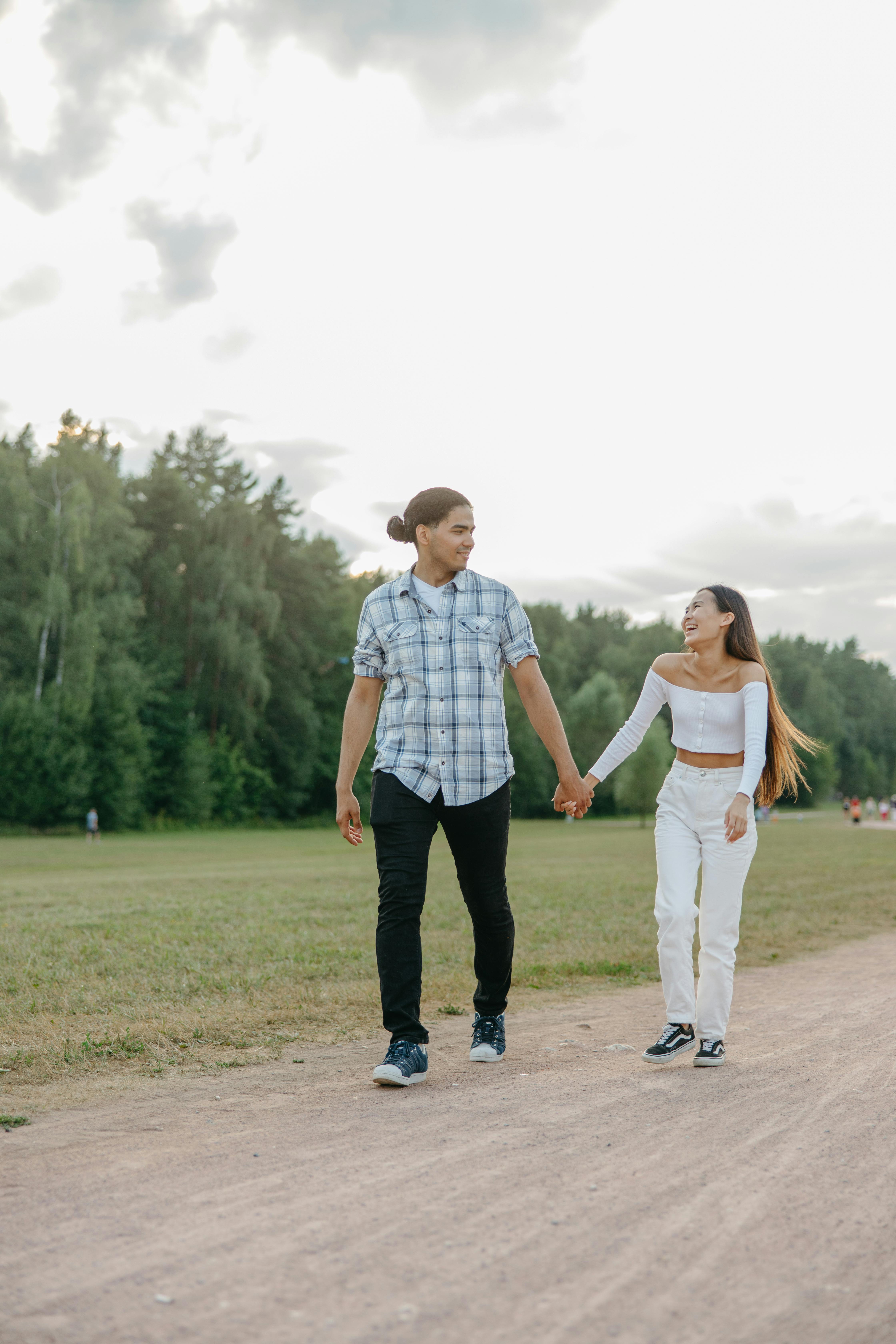 A young couple holding hands and walking happily on a park path surrounded by nature.