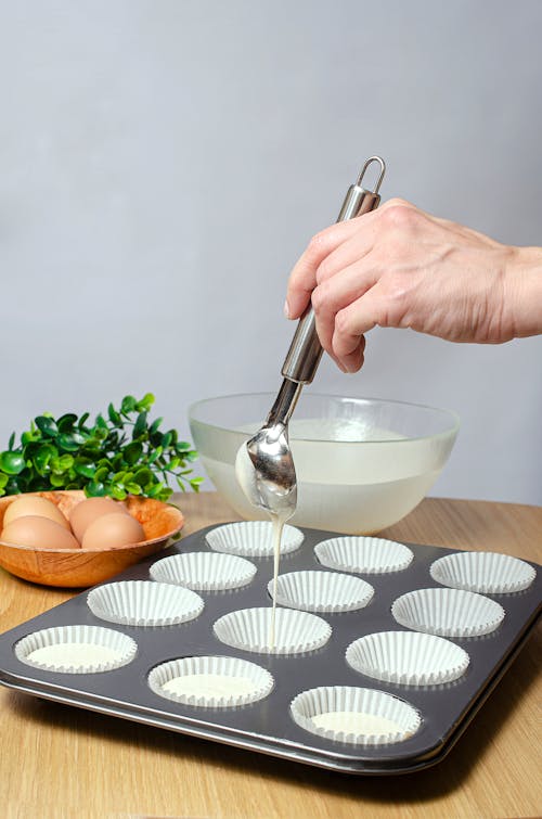 Hand of Person Pouring Batter Into Cupcake Holders