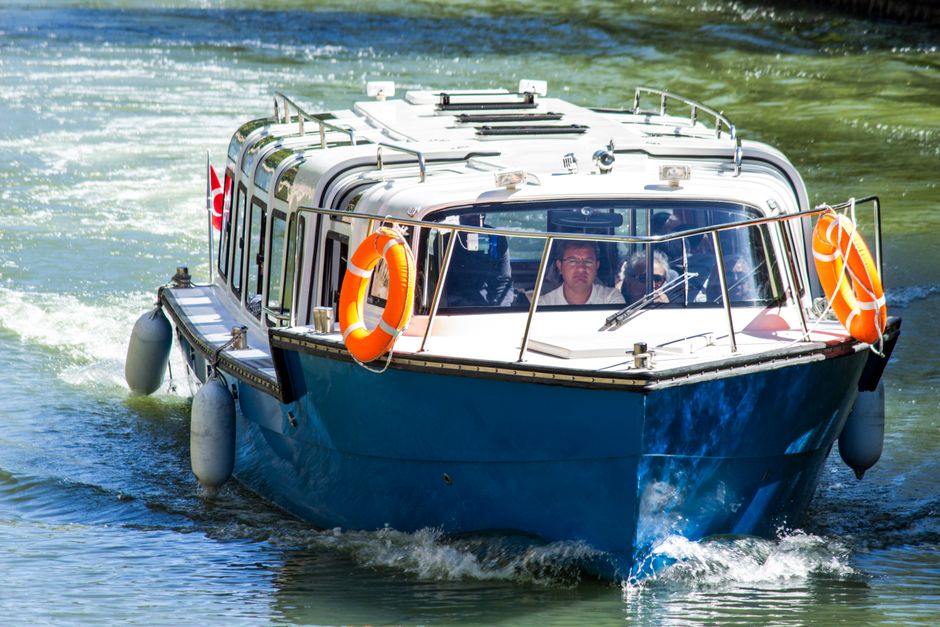 A vibrant blue motorboat cruising on a sunny lake with people onboard, featuring lifebuoys.