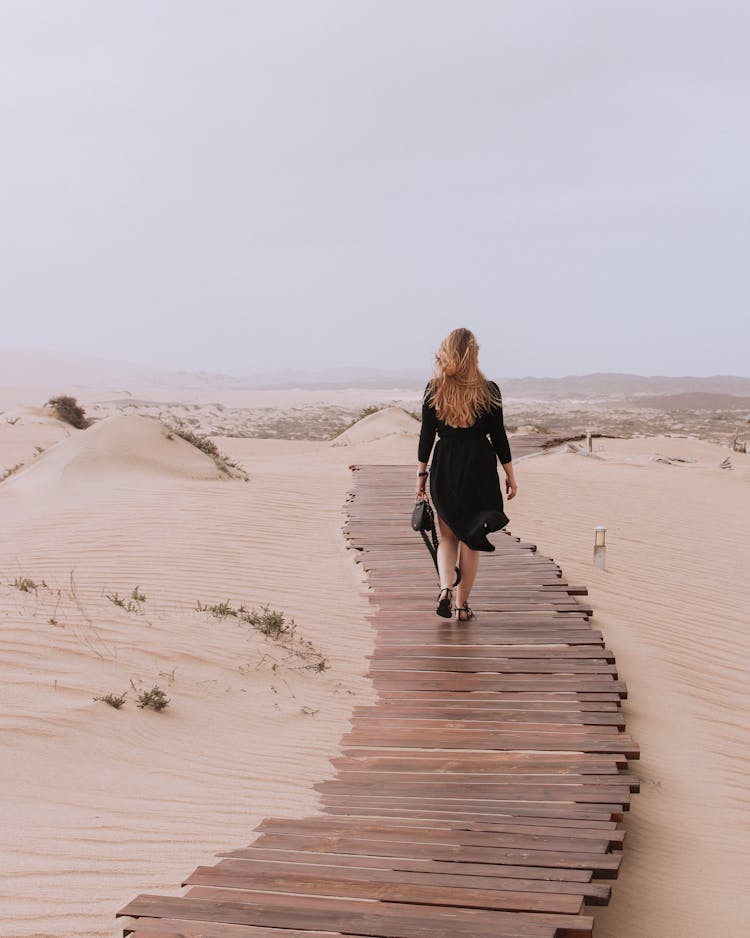 A Woman Walking Alone On A Wooden Pathway On A Desert