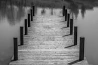 一张黑白图像中，喜怒无常的木码头延伸在平静的湖面上，倒映出清晰的倒影