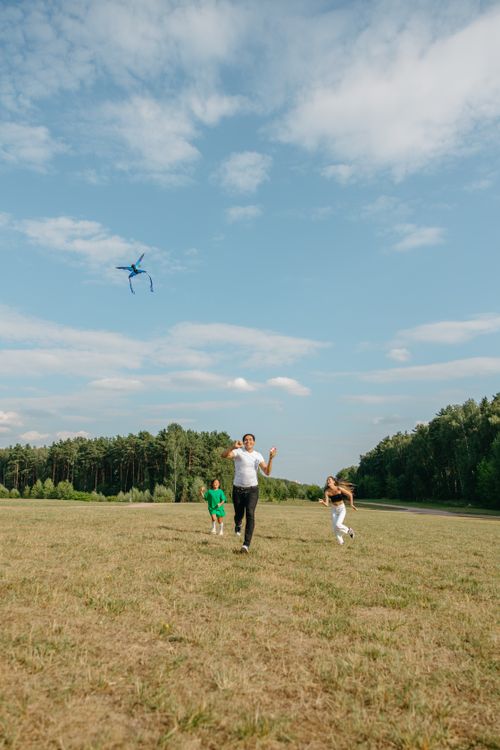 Free A family enjoys a sunny day flying a kite in an open grassy field with clear blue skies. Stock Photo