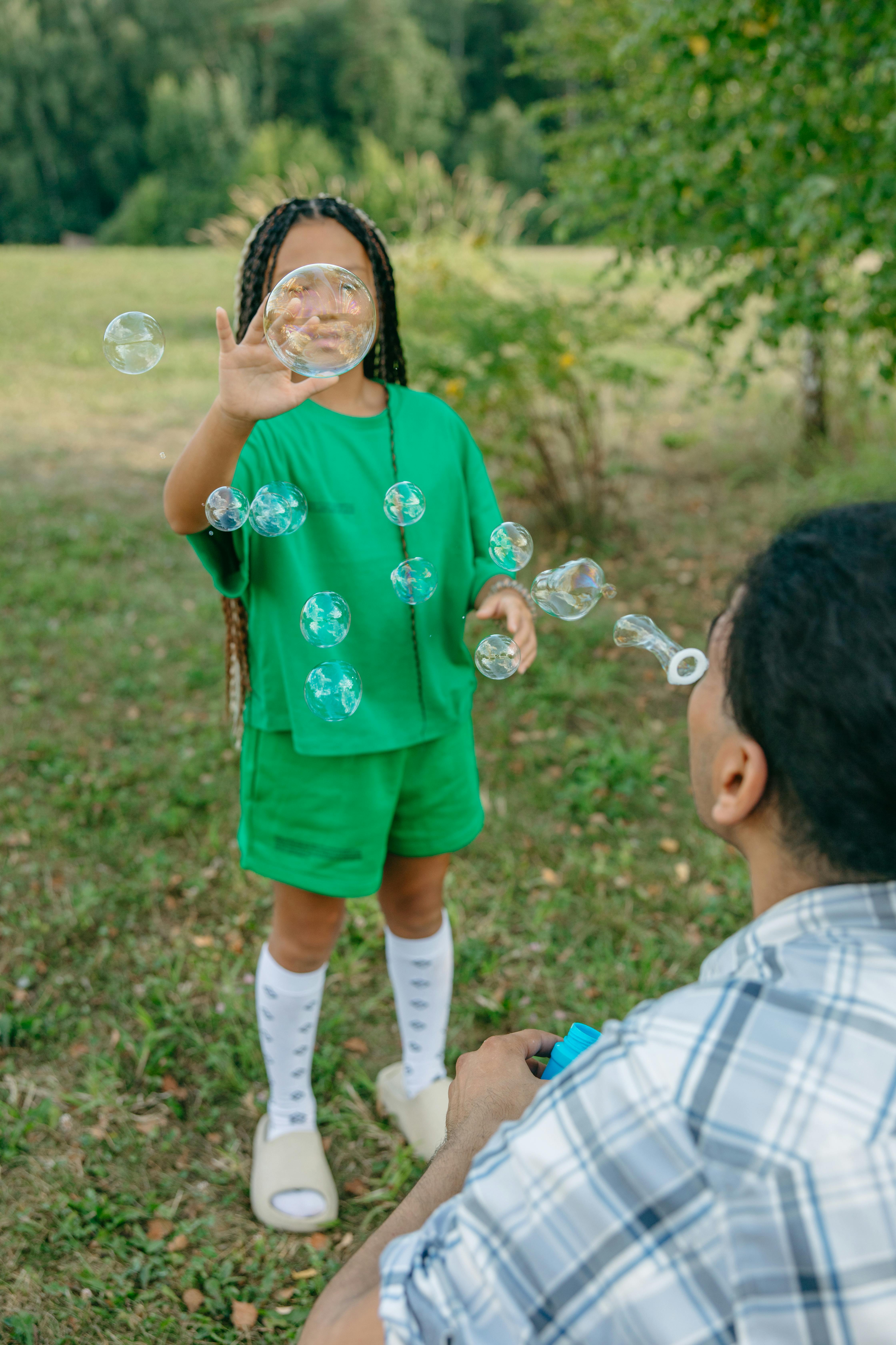 A joyful child interacts with bubbles in a lush green park, enjoying outdoor play.