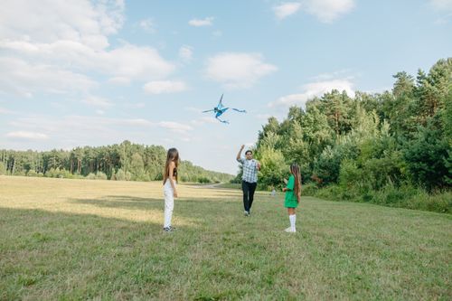 Free A man and two children enjoying a sunny day flying a kite in a vast grass field. Stock Photo