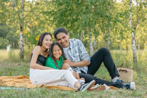 Free Cheerful family of three enjoying a picnic in a lush, green park. Stock Photo