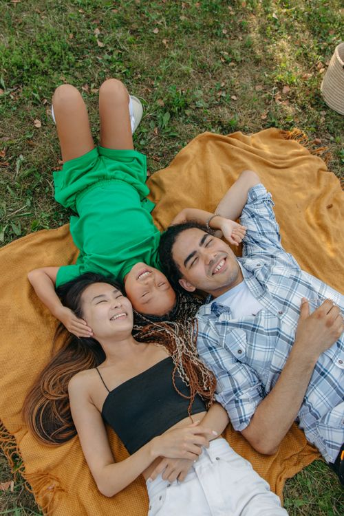Free Happy multiracial family lying on a picnic blanket, enjoying a sunny day in the park. Stock Photo