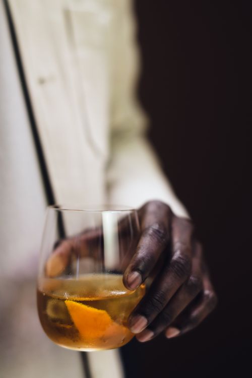 Free Close-up of a hand holding a whiskey glass garnished with orange peel, indoors with warm lighting. Stock Photo