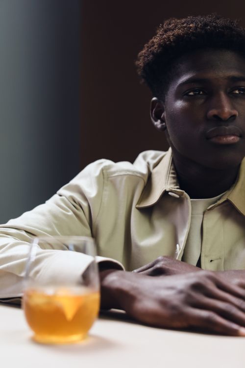 Free Man sitting at a table with a glass of liquor in focus, creating a thoughtful ambiance. Stock Photo