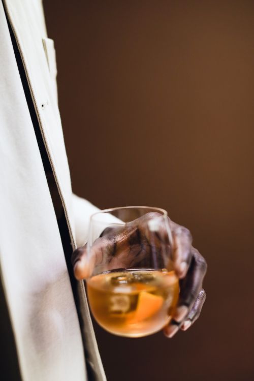 Free Close-up of an adult hand holding a glass of whiskey against a neutral background. Stock Photo