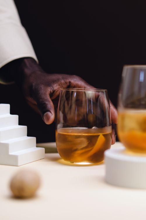 Free Close-up of a hand holding a whiskey glass on a white table, creating a sophisticated ambiance. Stock Photo