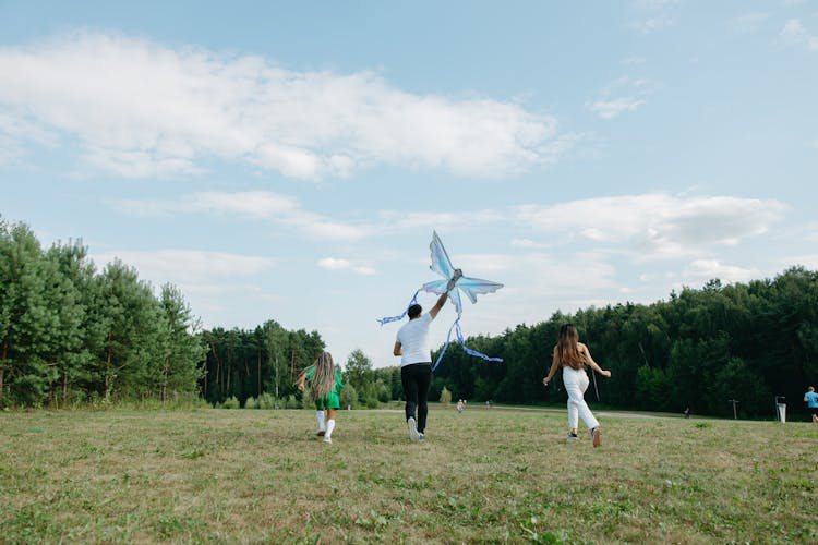 A Family Running On The Green Grass While Playing Kite