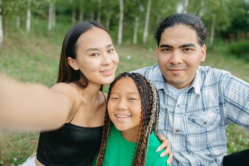 Free Smiling family of three enjoying a day in the park capturing a selfie together. Stock Photo