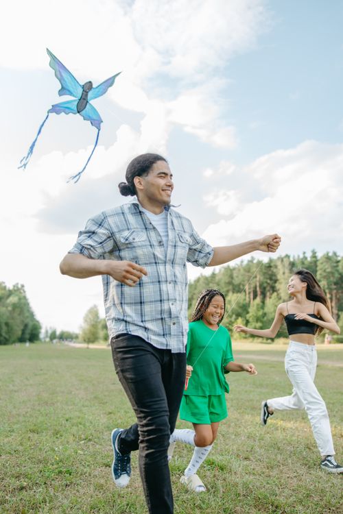 Free A joyful family running and flying a kite in a sunny park. Stock Photo