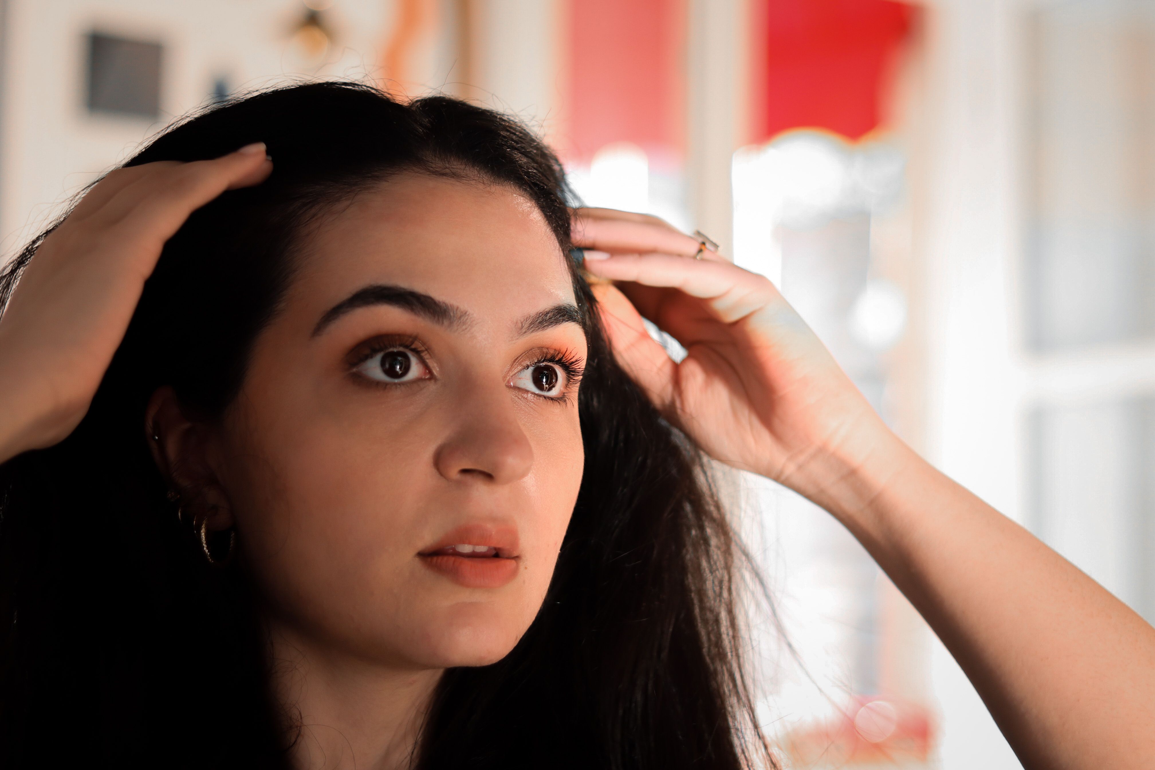 A young woman indoors touching her hair, captured in a warm, intimate setting.