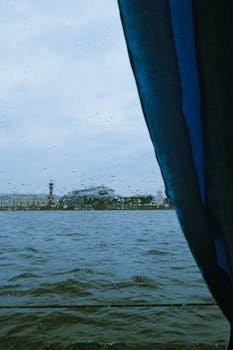 A rainy day view through a window capturing raindrops and a lakeside scene under a moody sky.