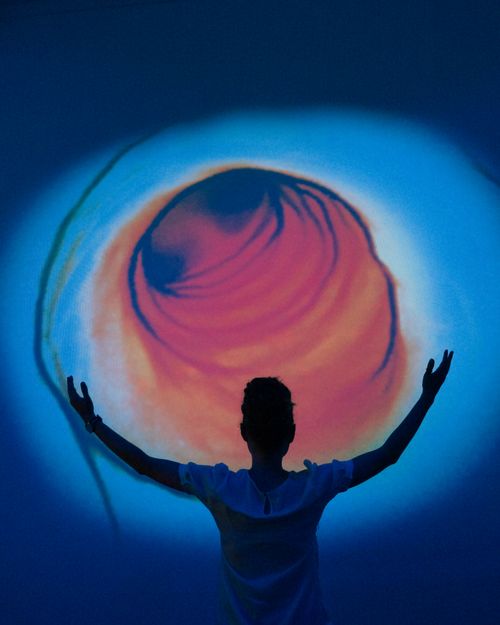Free Person silhouetted against a vibrant abstract projection with swirling colors evokes wonder and mystery. Stock Photo