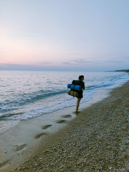 A Woman Walking at the Beach while Carrying a Rucksack