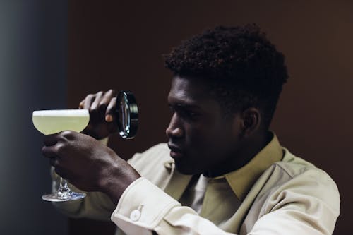 A Man Holding a Cocktail Glass and a Magnifying Glass