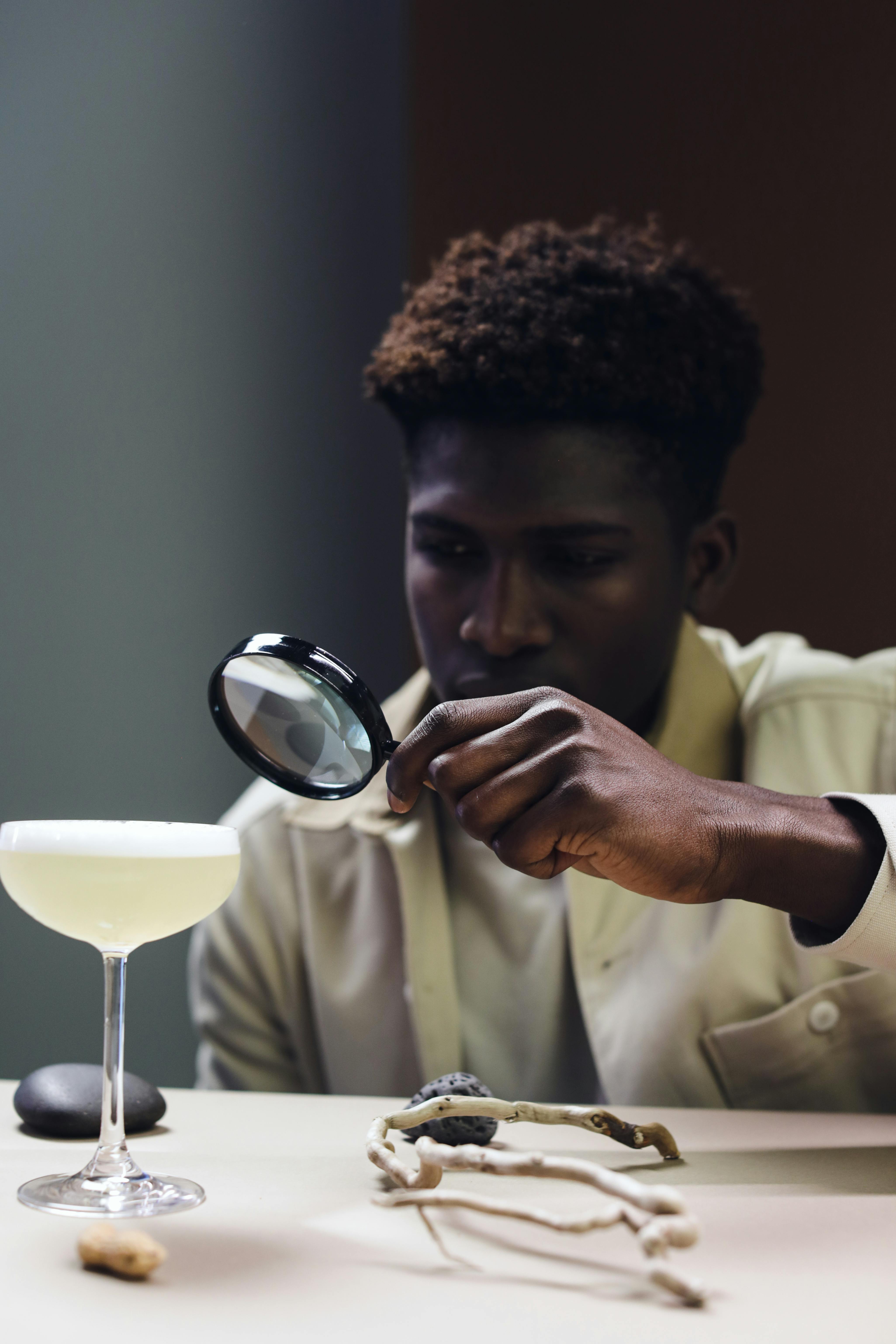 A Man Holding a Magnifying Glass Near a Drink