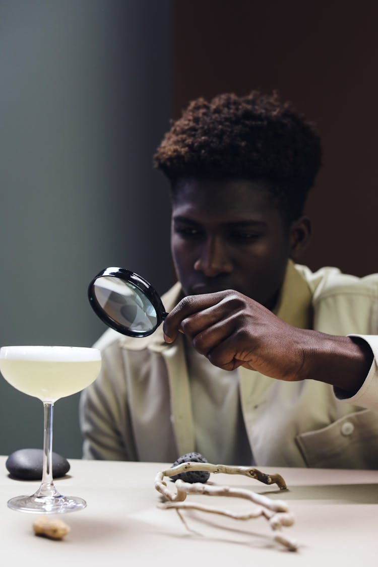 A Man Holding A Magnifying Glass Near A Drink