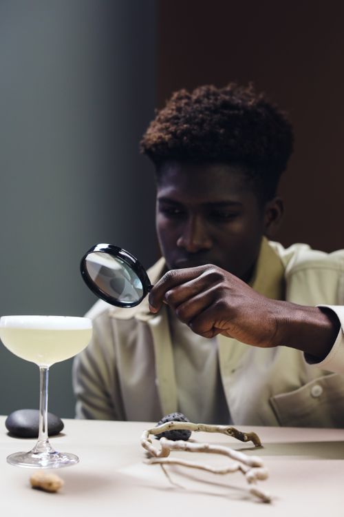 Free A man examines a cocktail with a magnifying glass, showcasing curiosity and focus. Stock Photo