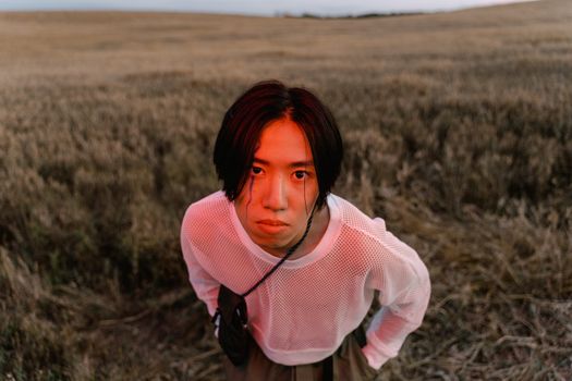 A striking portrait of a man in a fishnet top, standing in a field during twilight.