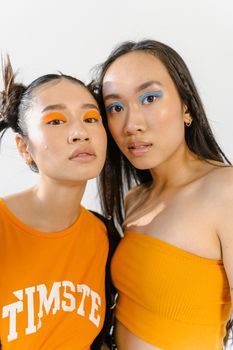 Colorful portrait of two women with bold makeup and stylish clothing against a neutral background.
