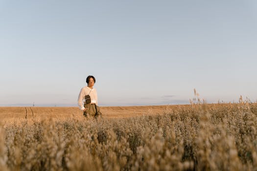 A fashionable individual standing in a vast wheat field at sunset. Warm tones and natural light create a serene atmosphere.