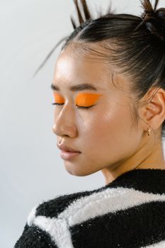 Close-up portrait of a young woman with orange eye makeup and striped sweater.