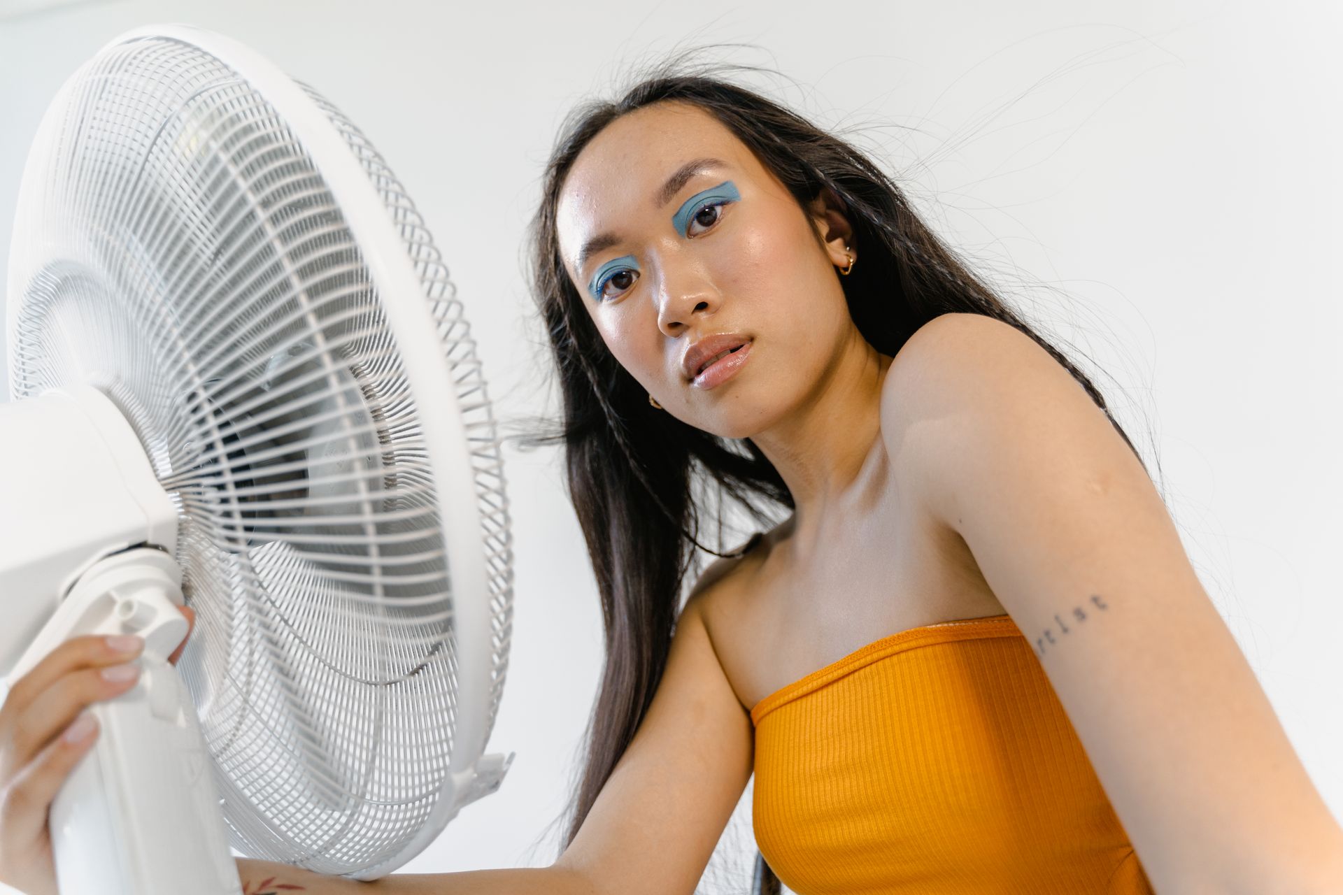 A Woman in Yellow Tube Top Holding an Electric Fan