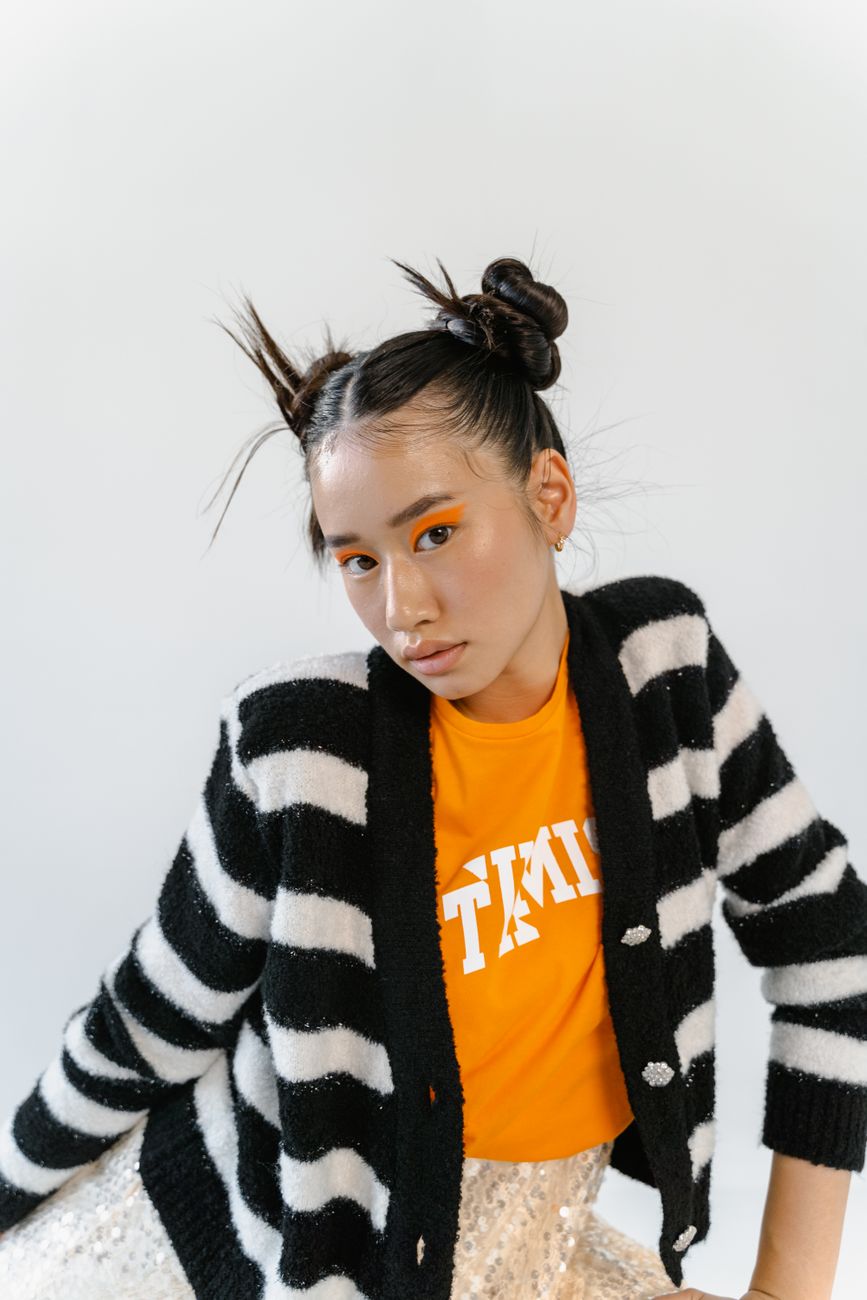 Portrait of a young woman showcasing bold eye makeup and unique hairstyle against a simple backdrop.