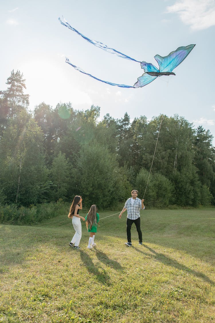 Father Flying A Butterfly Shaped Kite With Two Daughters