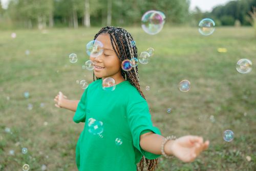 Free A girl with braided hair enjoys bubbles in a sunny park, exuding happiness and freedom. Stock Photo