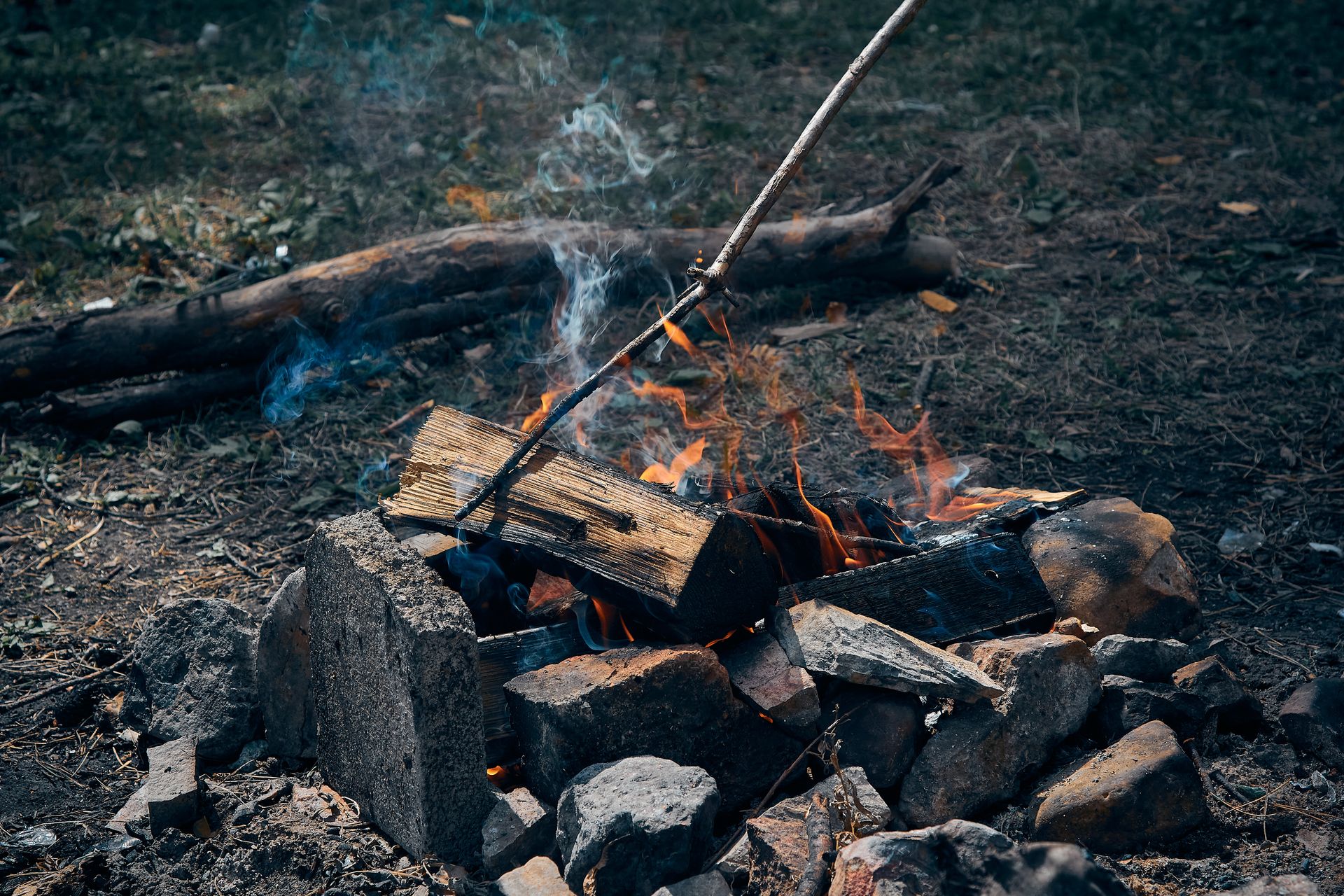 A cozy outdoor campfire burning with smoke and flames surrounded by nature.