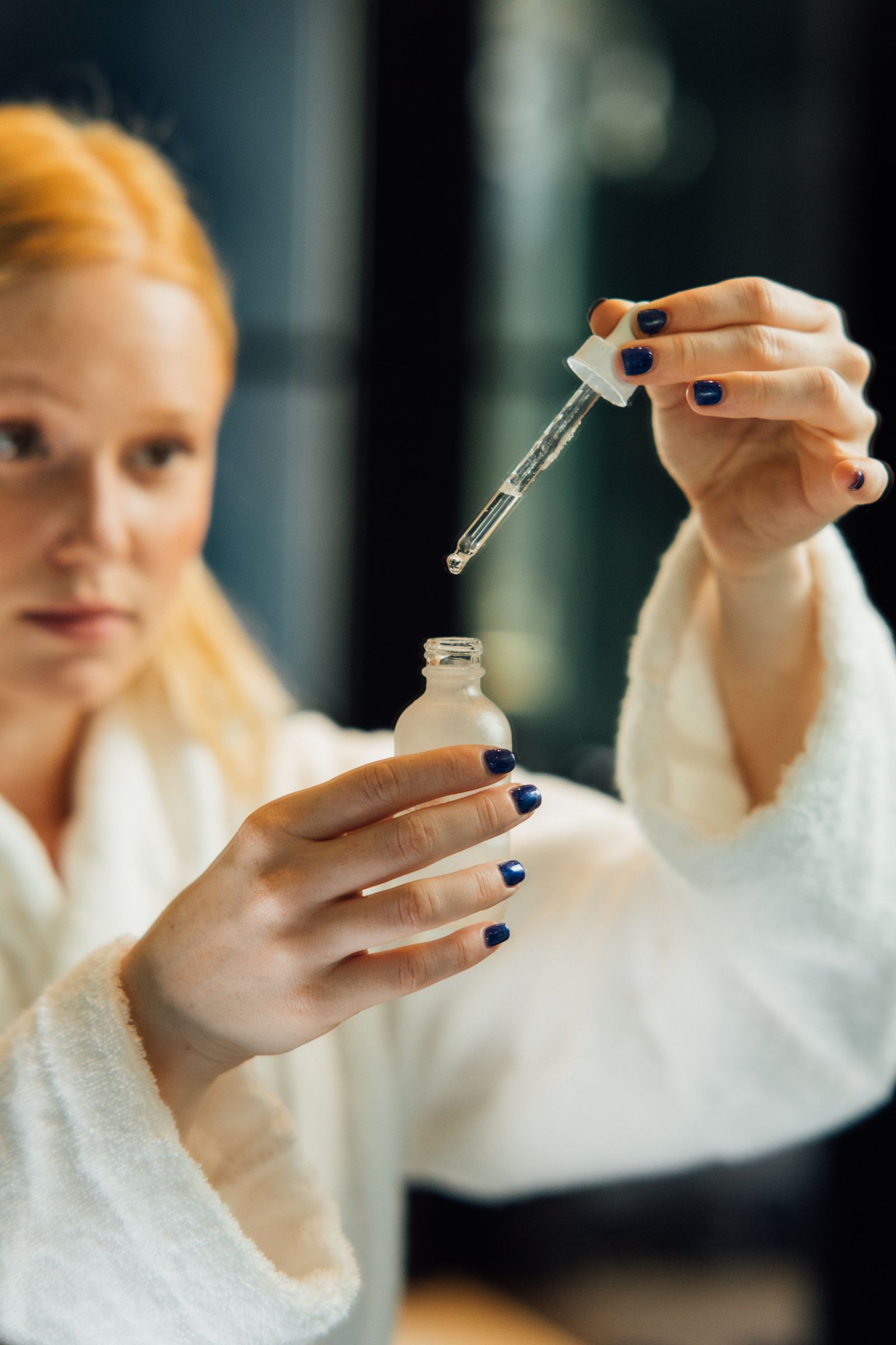 Woman in a white robe holding a skincare product.