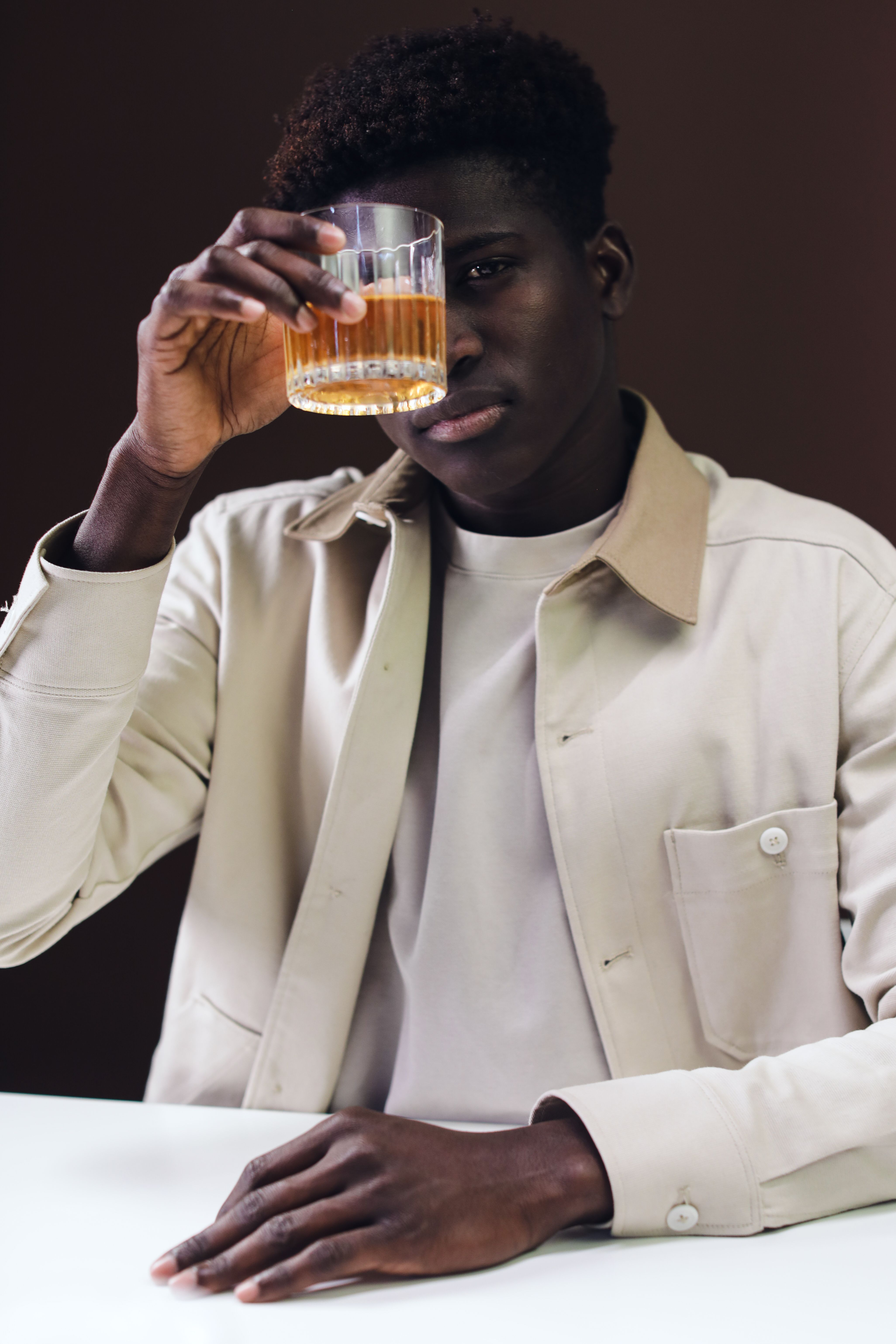 Portrait of a man in a beige jacket holding a whiskey glass, conveying a sophisticated lifestyle.
