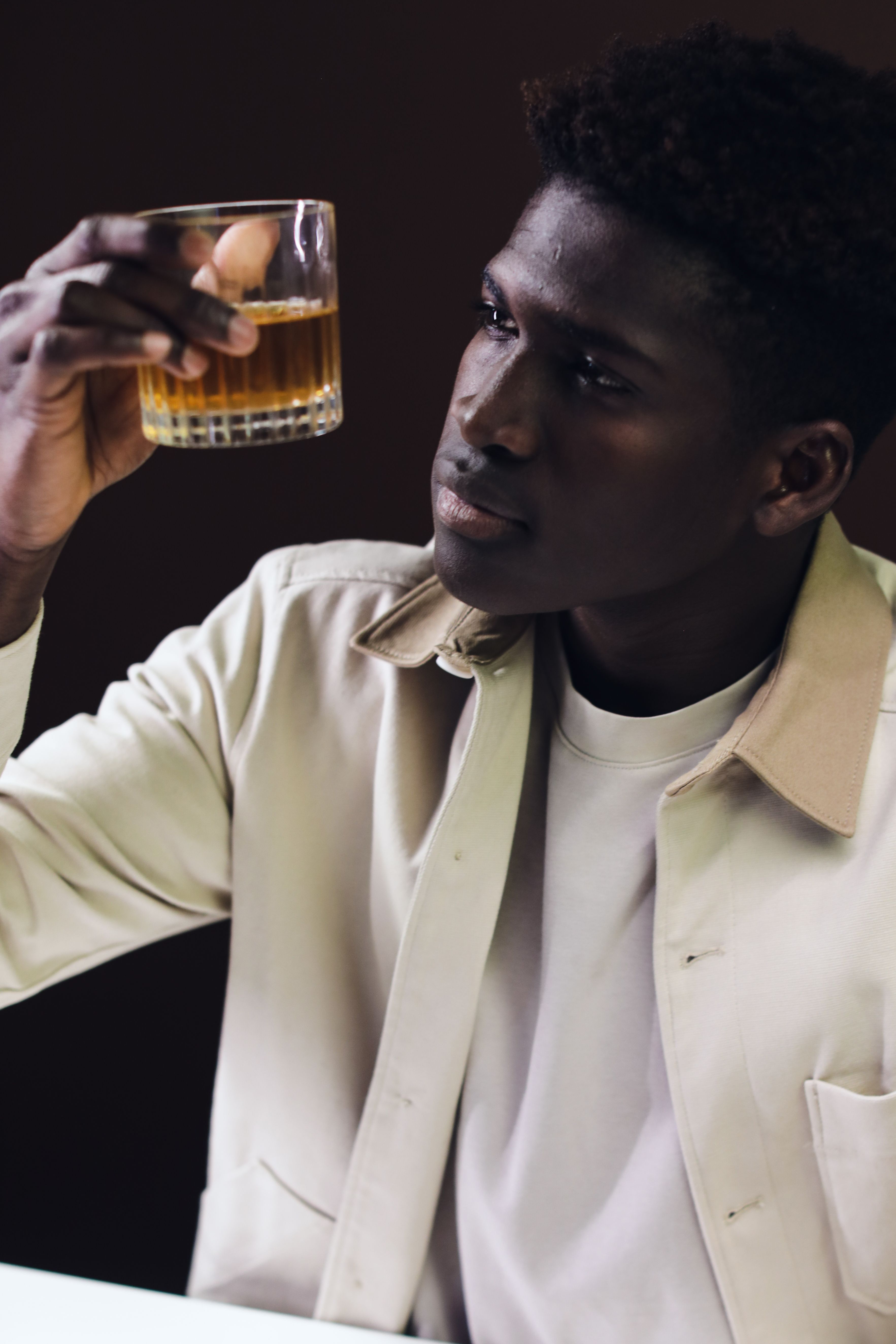 A contemplative man holds up a glass of whiskey, evaluating its contents closely.