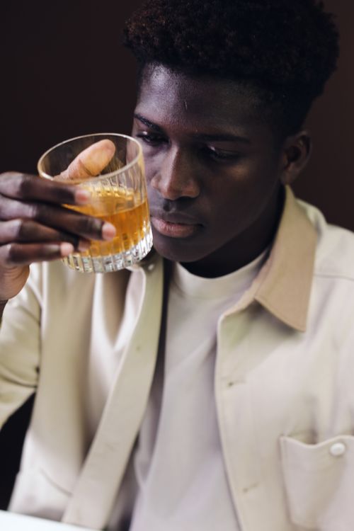 Free Young man in a shirt examining a glass of whiskey with focused expression. Stock Photo