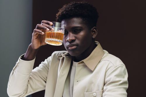 Free A young man with afro hair holding a whisky glass indoors, enjoying a moment of reflection. Stock Photo