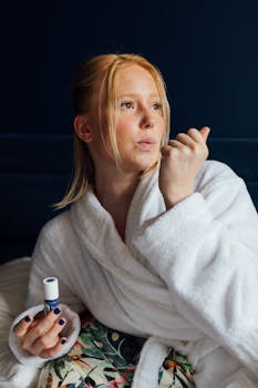 Blonde woman in white robe applying nail polish indoors, capturing a moment of self-care and relaxation.