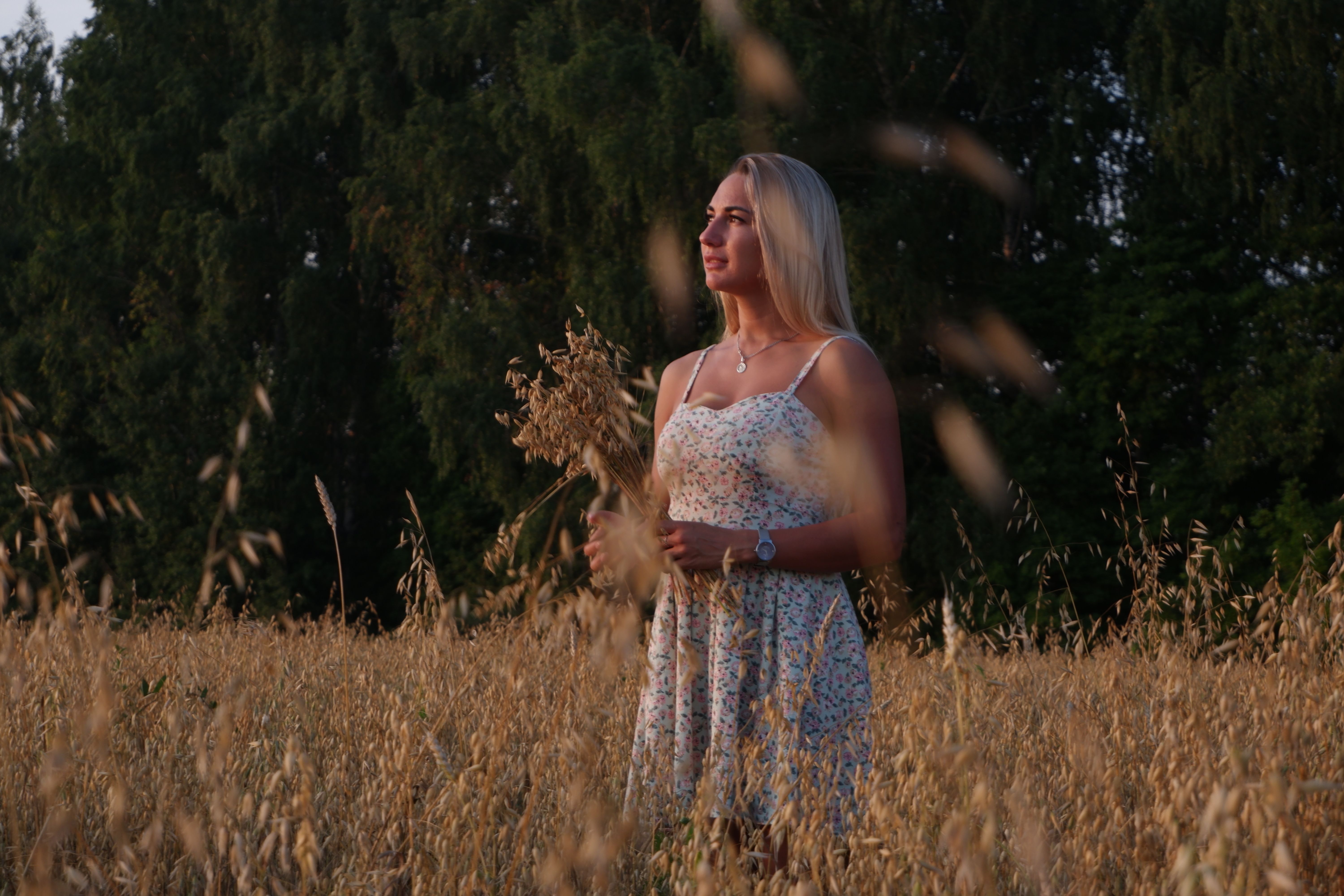A woman stands in a wheat field, holding grains under a clear summer sky.