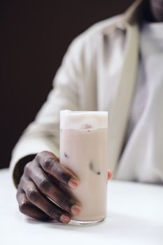 Close-up of a hand holding a frothy iced coffee in a clear glass.