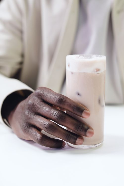 Free A close-up of a person holding a glass of iced coffee with creamy texture. Stock Photo
